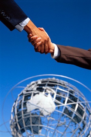 handshake representing global collaboration against a metallic globe and bright blue sky.