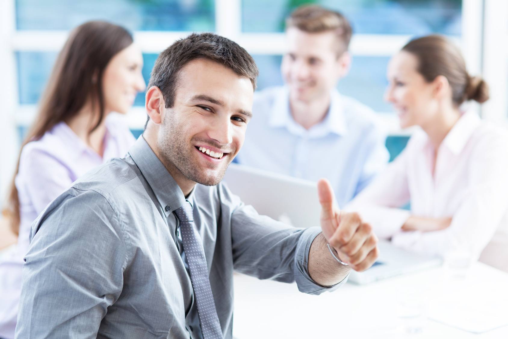 smiling young man in a grey shirt promotes teamwork in a bright, modern office.