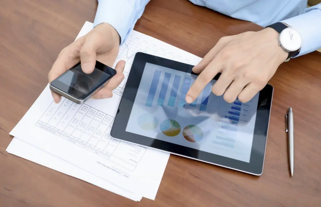Virtual Desktop Vs Web Apps: Which Should You Choose? 6 person analyzing data on tablet with smartphone, papers, and pen in modern workspace.