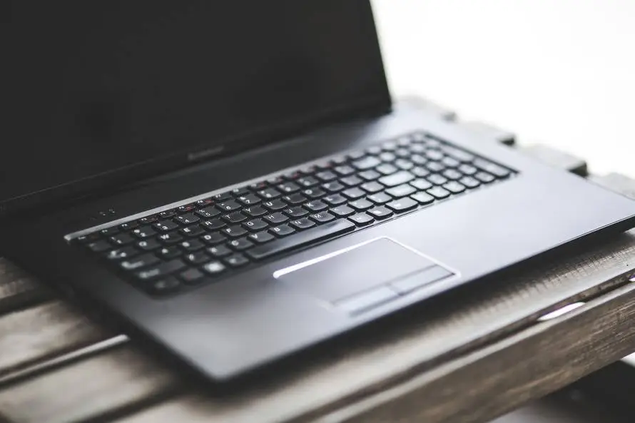 Is Outsourcing It Support Right For Your Business? 3 sleek black laptop on rustic wood, blending modern technology with natural warmth.