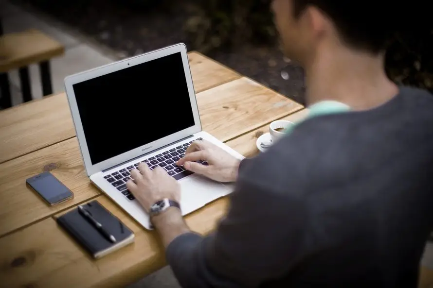 young man working on a laptop outdoors, blending productivity and relaxation in a café setting.