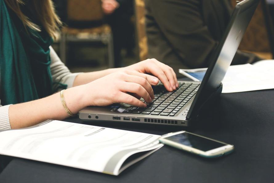 hands typing on a laptop in a collaborative modern workspace with notes and a smartphone.