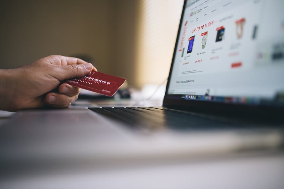 dynamic online shopping scene with a hand holding a red credit card and a glowing laptop.