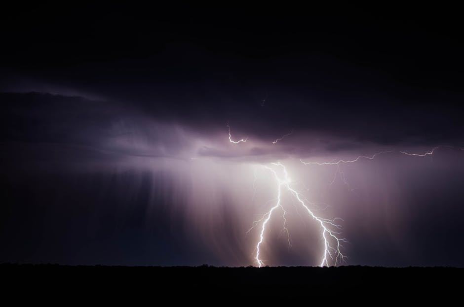 dramatic lightning strike illuminates dark clouds above a shadowy field during a nighttime storm.