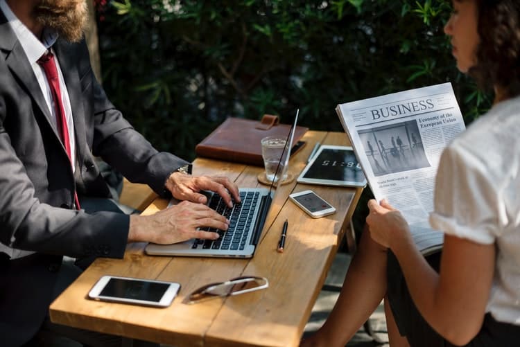 a man in a suit and a woman read a newspaper during an outdoor meeting.