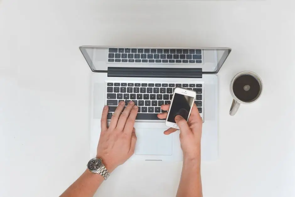 Use The Right Network Support To Prevent Cyber Crimes At Your Business 8 a person multitasks on a laptop while holding a smartphone in a modern workspace.