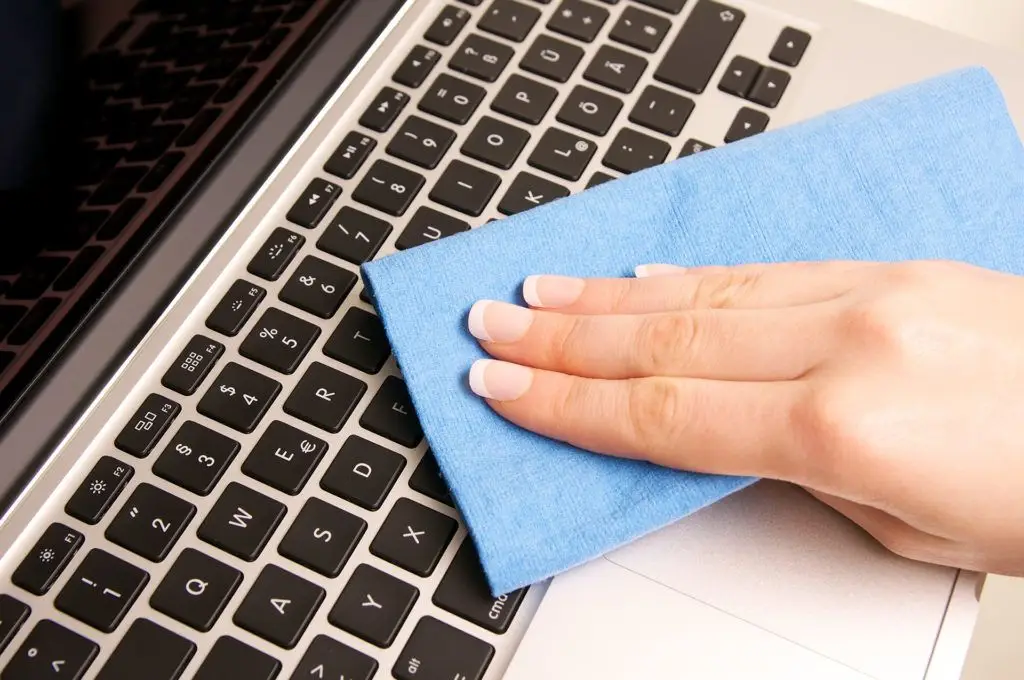 Keep Your Keyboard Clean - Computer Tip Of The Day 1 hand using a microfiber cloth to clean a sleek laptop keyboard for better maintenance.