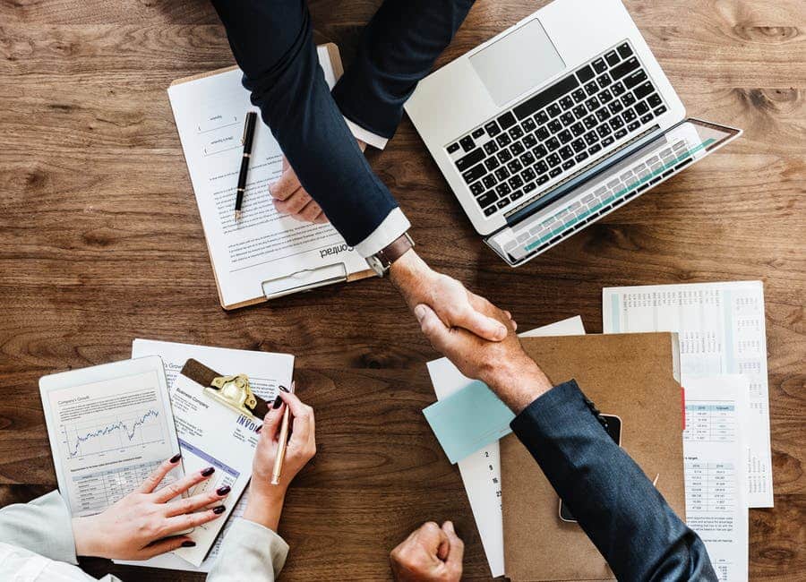 handshake symbolizing partnership in managed services amid organized documents and a laptop.