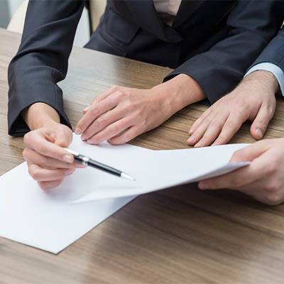 close-up of hands signing documents during a professional negotiation at a wooden table.