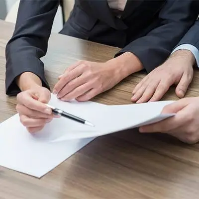 close-up of hands signing documents during a professional negotiation at a wooden table.