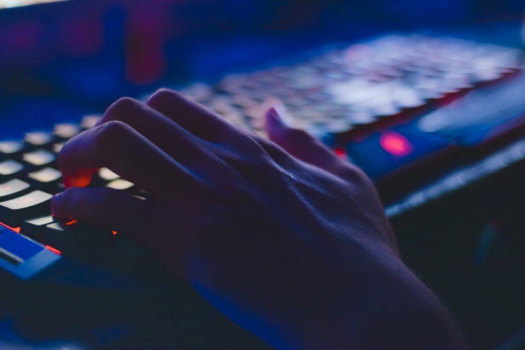 focused hand hovering over an illuminated keyboard in a blue-lit digital environment.