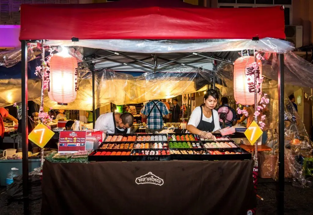 A Partner Is More Than Just A Product Vendor 3 colorful sushi stall at a lively night market, with a focused vendor and festive atmosphere.
