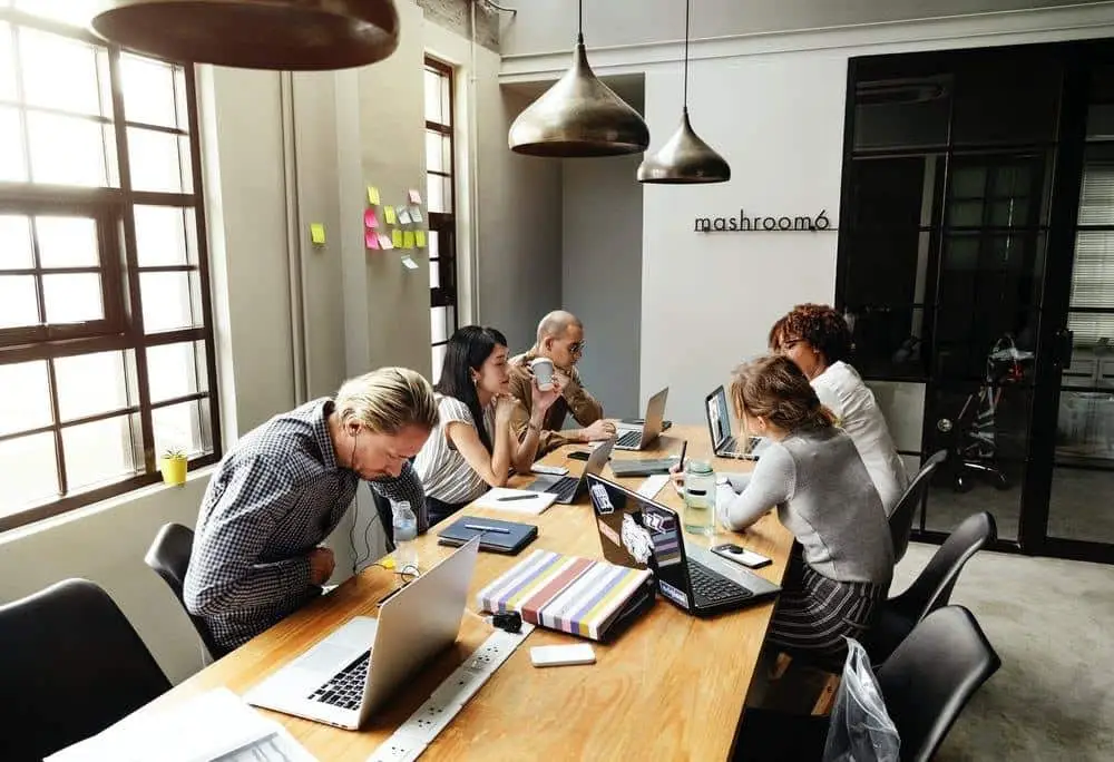 diverse professionals collaborating in a modern workspace with laptops, warm lighting, and creative decor.
