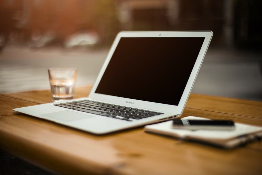 modern laptop on rustic table with water tumbler and mobile phone for a creative workspace.