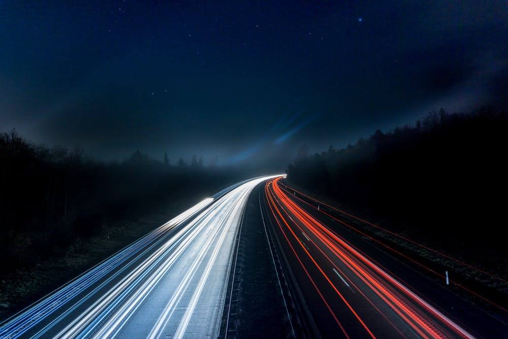 long exposure nighttime highway photo showcasing vibrant vehicle light trails and a serene landscape.