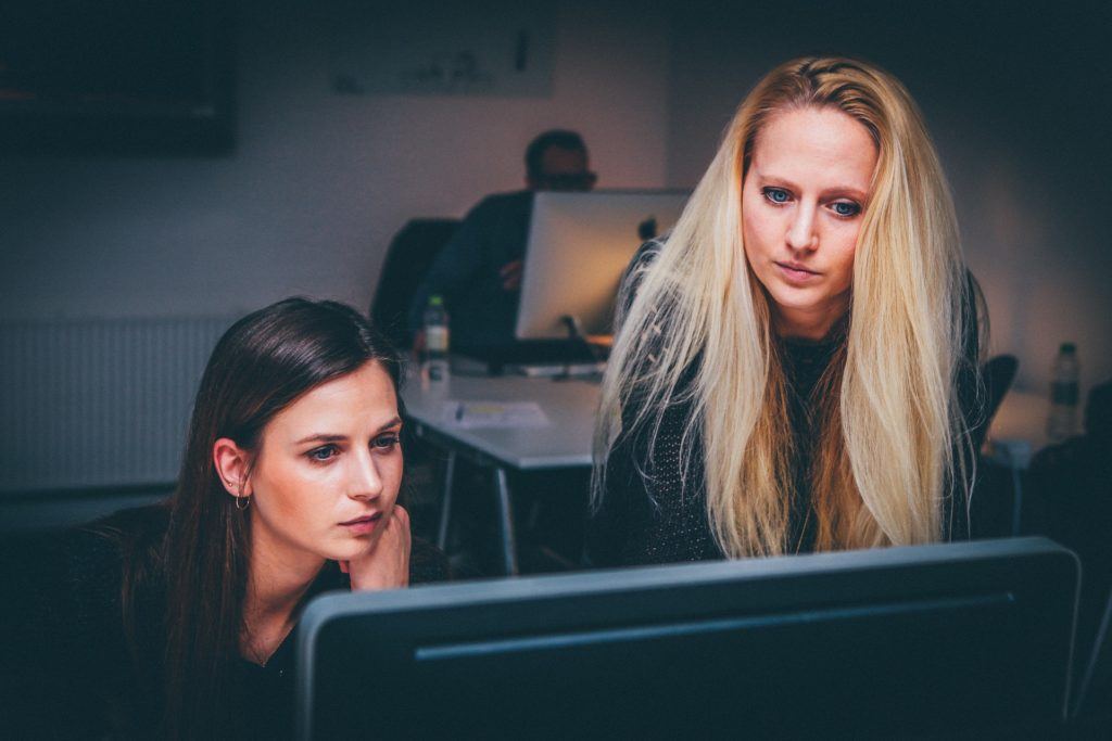two women collaborating at a computer in a modern, creative workspace.