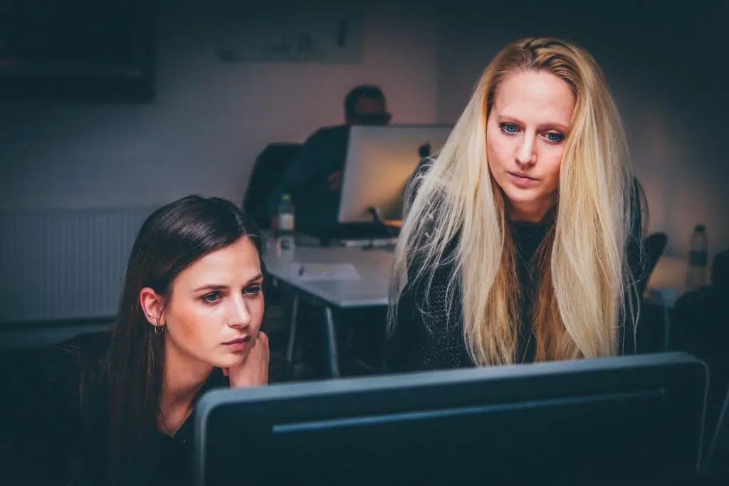 two women collaborating at a computer in a modern, creative workspace.