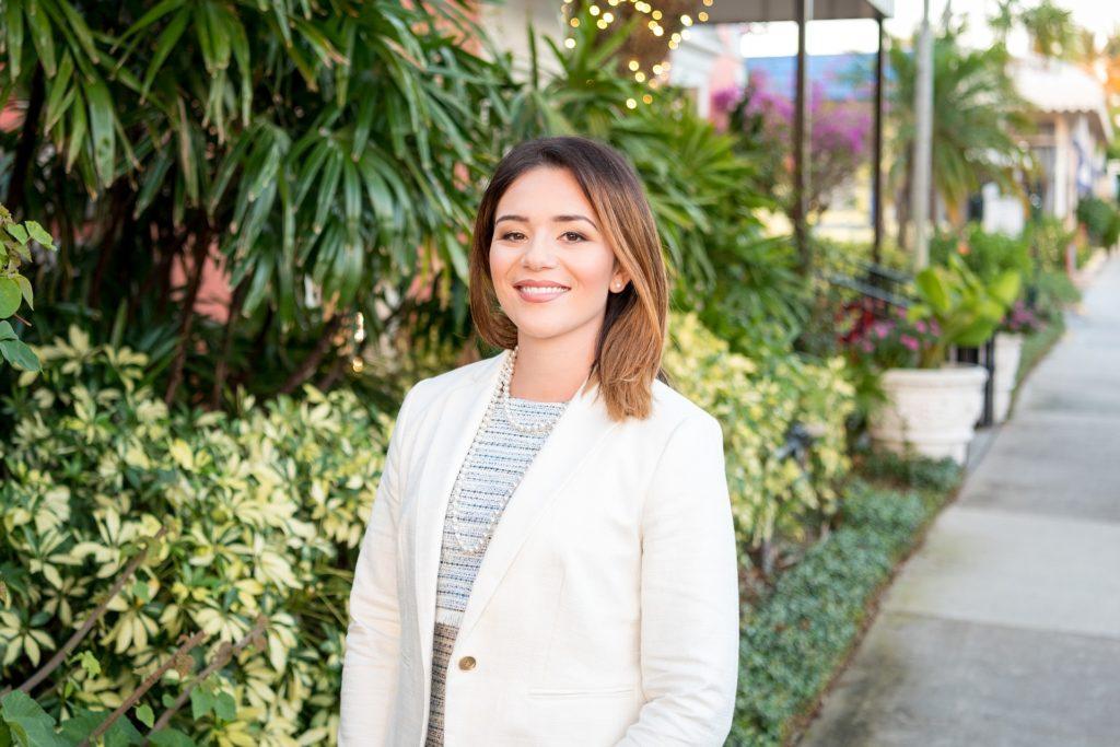 confident professional woman in a white blazer, surrounded by vibrant greenery and flowers.