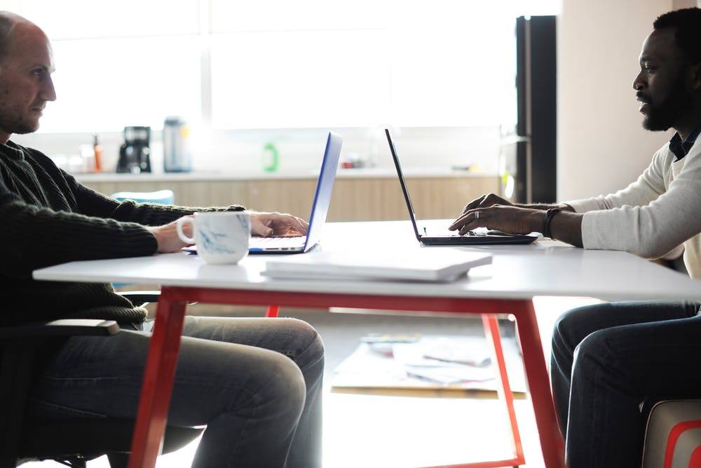 two professionals collaborate in a bright, modern workspace with laptops and a vibrant table.