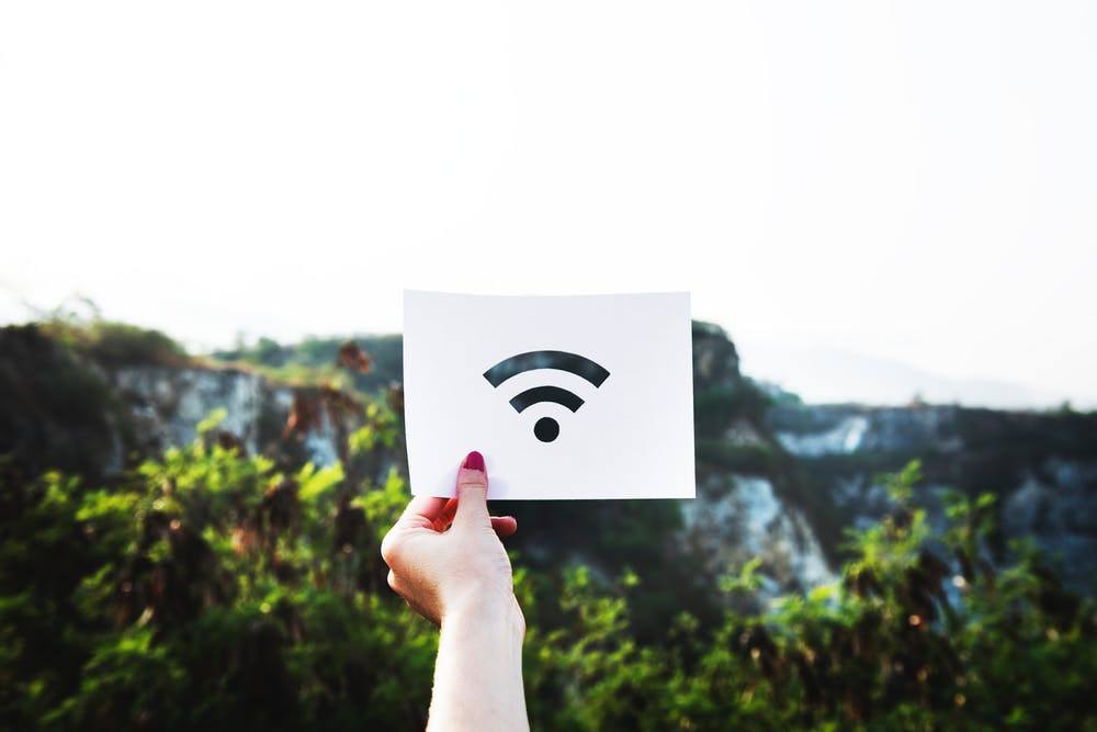 a hand holding paper with a wi-fi symbol against a serene natural background.