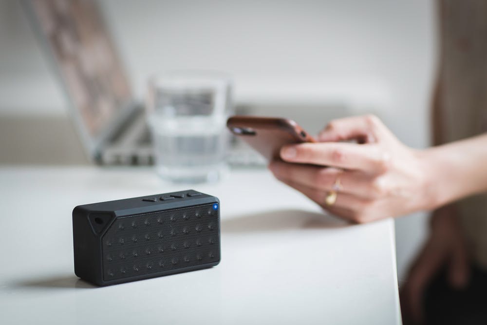 sleek black bluetooth speaker with smartphone, laptop, and water in modern workspace setting.