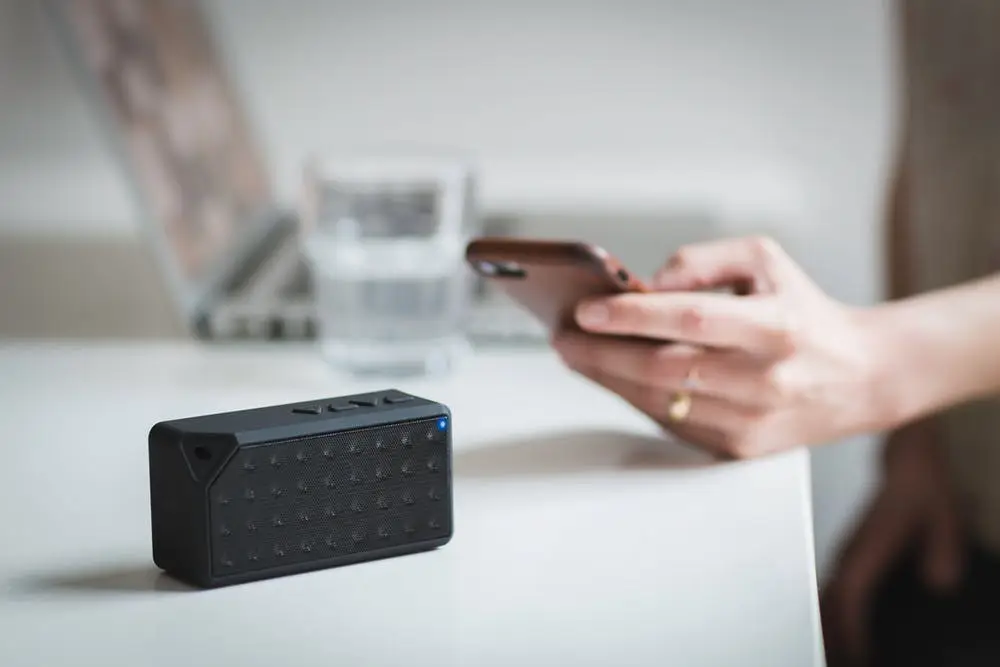 Is Your Business Wifi Network Secure? 1 sleek black bluetooth speaker with smartphone, laptop, and water in modern workspace setting.
