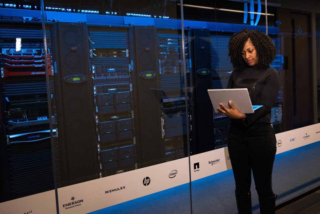 professional woman engaged with technology in a modern server room filled with active servers.