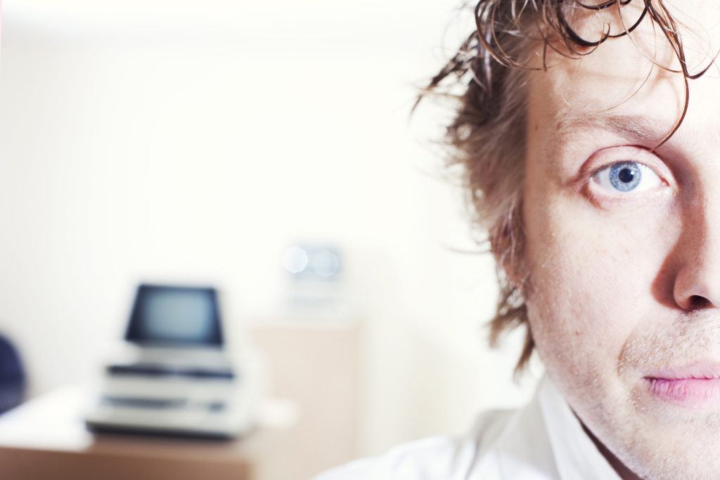 contemplative man with striking blue eyes in a softly lit workspace, embodying curiosity.