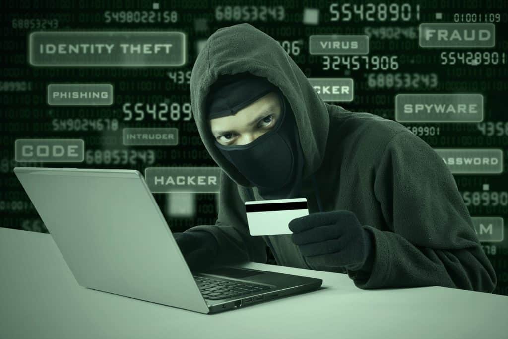 hacker in hoodie and mask focused on laptop, highlighting holiday season cybersecurity risks.