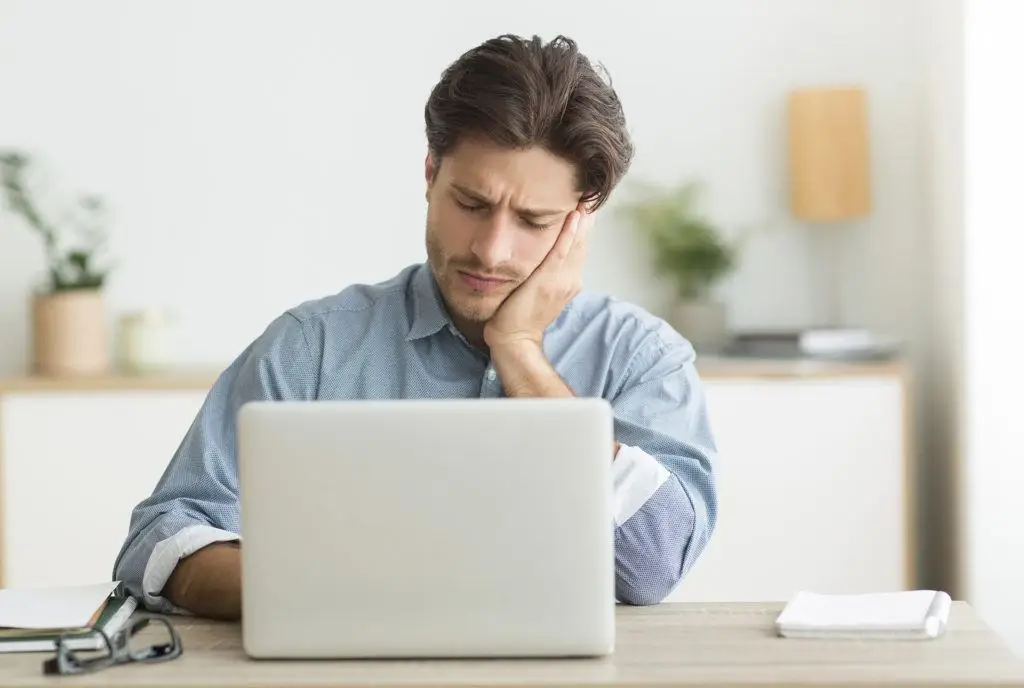 Why Are We Weary Of Emerging Technologies? 3 young man in a blue shirt deep in thought at a laptop in a serene workspace.