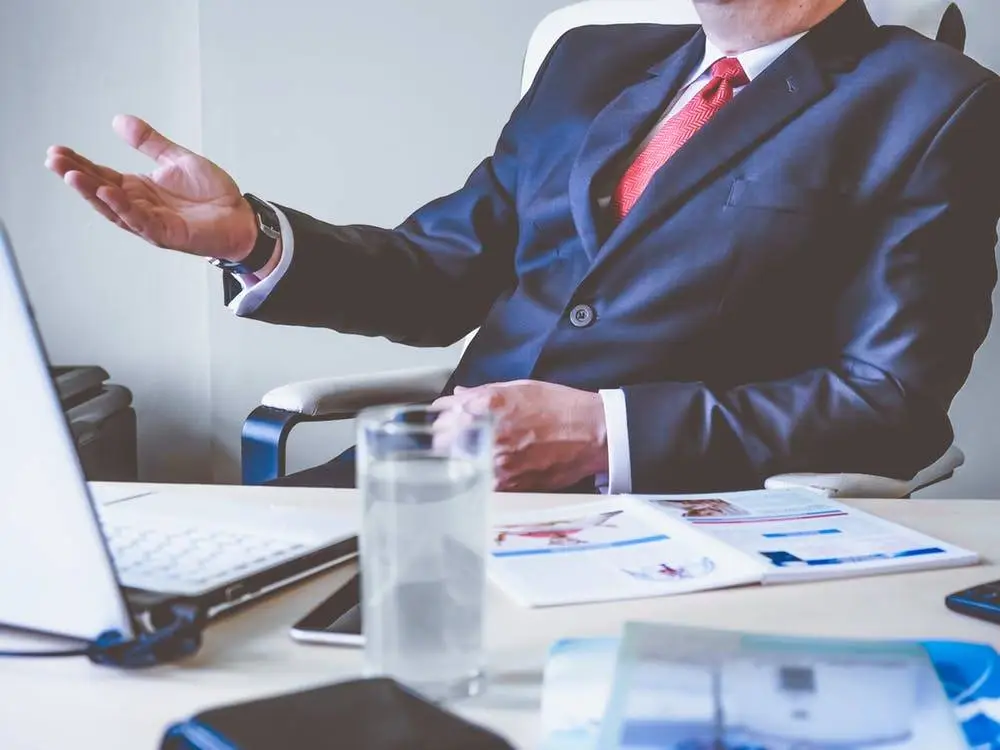 Why Patch Management Is Important In 2019 And Beyond 4 confident businessman discussing patch management at a modern desk with a laptop and documents.
