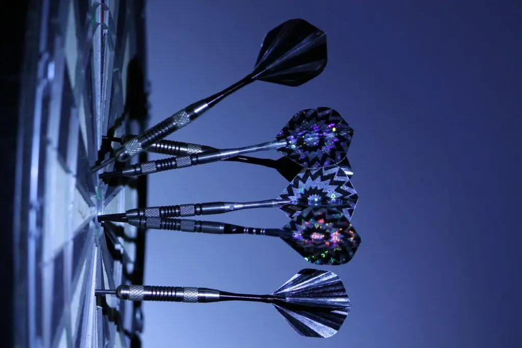 Hackers Target Businesses: Owners 12X More Likely To Be A Cyber Target 4 darts expertly aimed at a dartboard, highlighting precision in competitive gameplay against a blue backdrop.