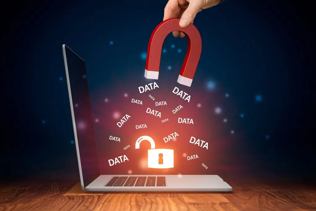 a hand holds a red magnet above a laptop, symbolizing data retrieval and security.
