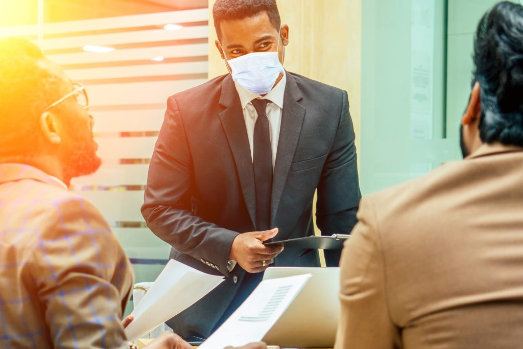 men in suits discuss documents during a safe business meeting with face masks.