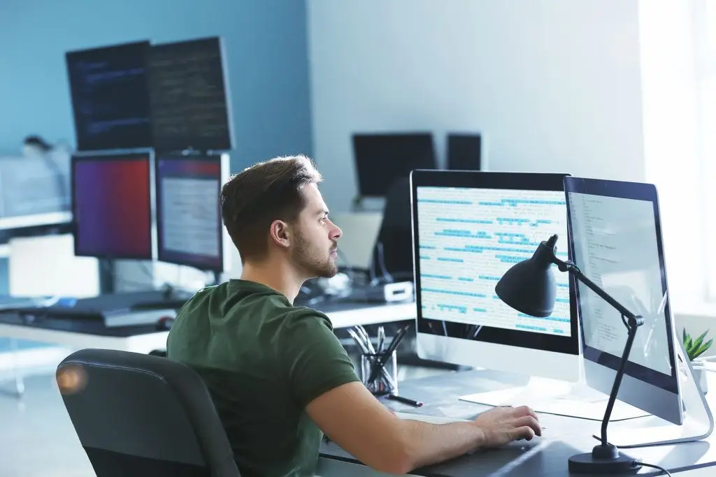 Aspects Of Managed Services Support 5 young programmer coding at a modern workstation with multiple screens and natural light.