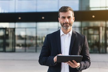 confident professional in a suit holding a tablet outside a modern corporate building.