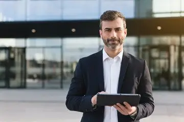 confident professional in a suit holding a tablet outside a modern corporate building.