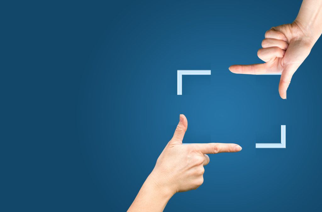 two hands create a rectangular frame against a vibrant blue background, representing artistic expression.