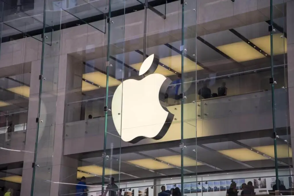 Are Apple'S Devices Really More Secure? 5 illuminated apple logo on a sleek storefront with shoppers inside a modern retail space.