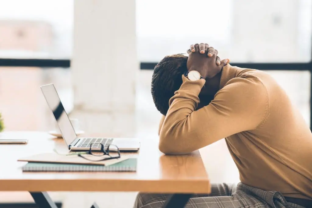 man in beige sweater reflecting on stress in a bright, urban workspace.
