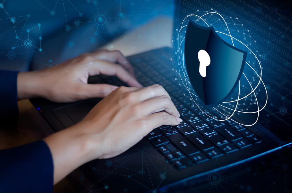 focused hands typing on a laptop, emphasizing cybersecurity and data protection through a digital shield.