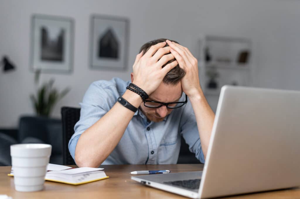 stressed businessman at desk, overwhelmed by chaos of workplace burnout and challenges.