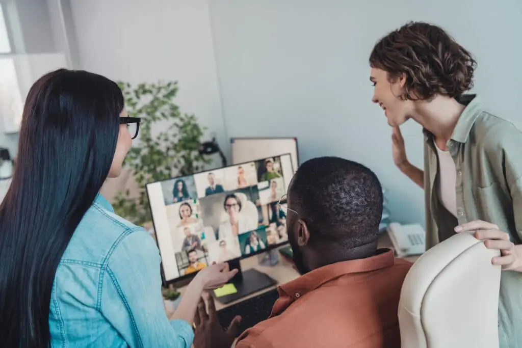 Company Culture With Hybrid Work 1 diverse team collaborates around a computer in a hybrid workspace, engaging in a video call.