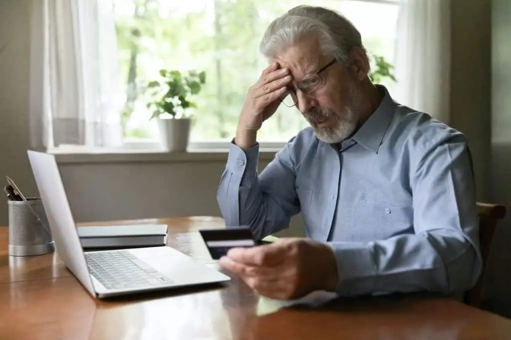 elderly man anxiously reviewing finances, concerned about online payment security and financial fraud risk.