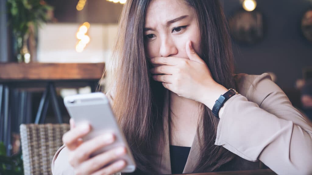 young woman in café reacts with concern while reading troubling news on her smartphone.